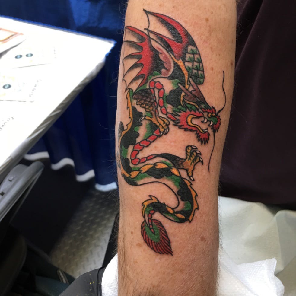 A green, red, and yellow dragon tattoo on an arm. 