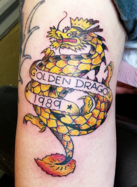 Golden dragon tattoo on caucasian arm. Date reads 1989. 