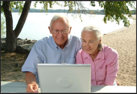 two elderly people smiling at a computer screen outside