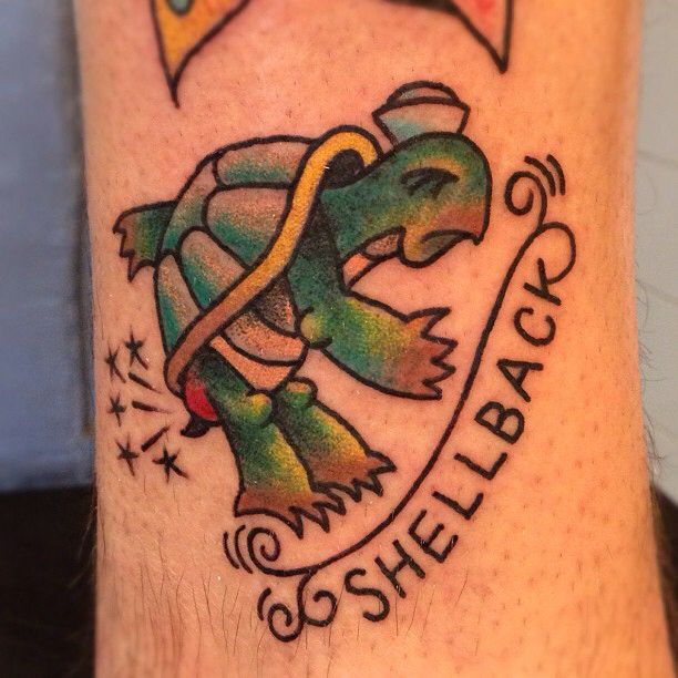 A turtle tattoo with text reading shellback underneath it on the arm of a man