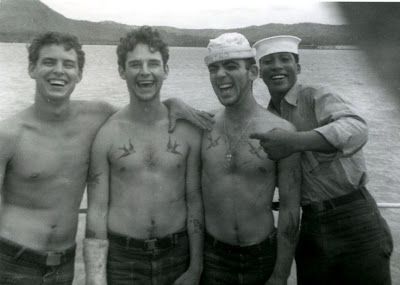 A black and white photo of four young men, two with swallow tattoos. 