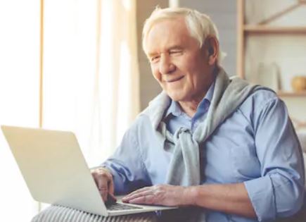 Senior citizen in a blue button up shirt on his laptop at home