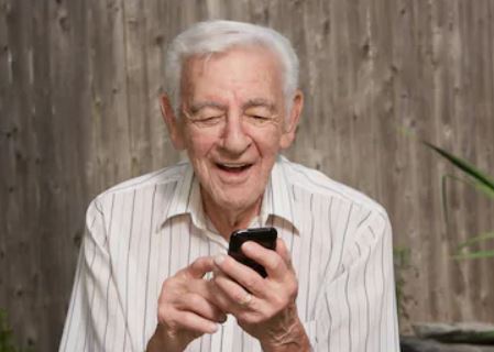 Senior citizen smiling down at his mobile phone 