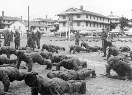 Basic training recruits do push ups outside, overlooked by drill sergeants. 